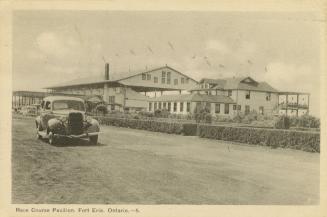 Black and white photograph of a car on a track with buildings behind it.