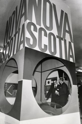 Two men seen through round hole in display cube decorated with the words, 'Nova Scotia.'