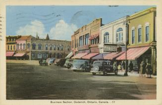 Colorized photograph of automobiles parked beside the sidewalk of a downtown area.