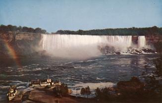 Color photograph of rapids in front of a large waterfall. 