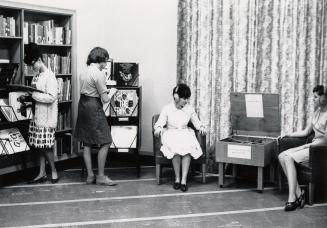 Picture of interior of library. Two women standing looking a vinyl records and two women wearin ...