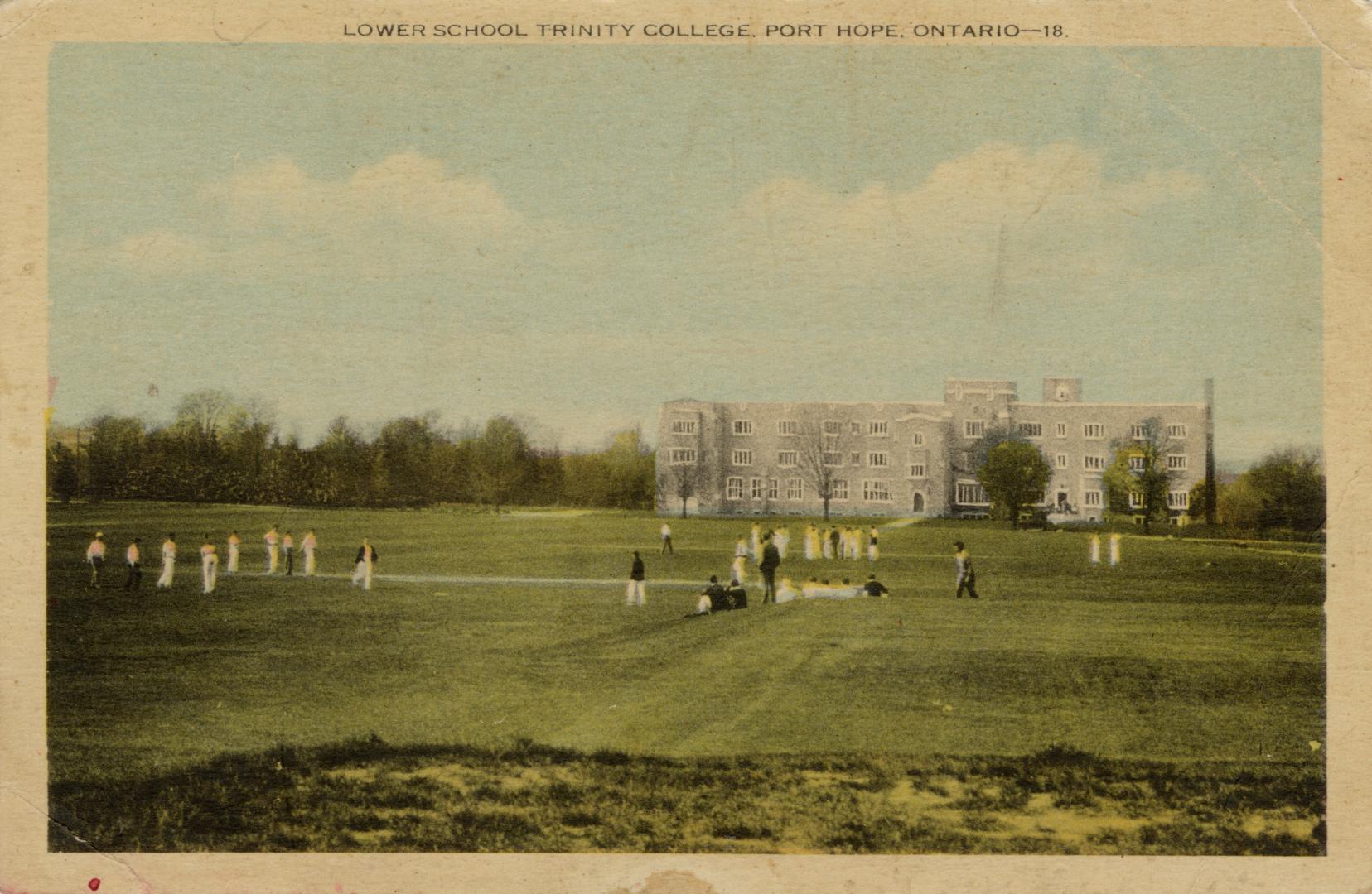 Colorized photograph of boys dressed in white on a cricket pitch in front of a large building.