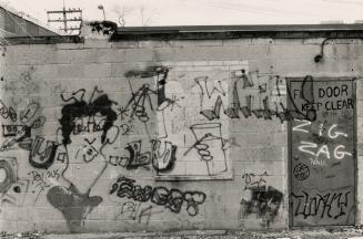 Cinder block wall with scribbles, a comic face, two hands holding tumblers