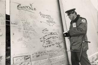 Industrial door with words and scribbling on it. Policeman standing beside it taking down notes…