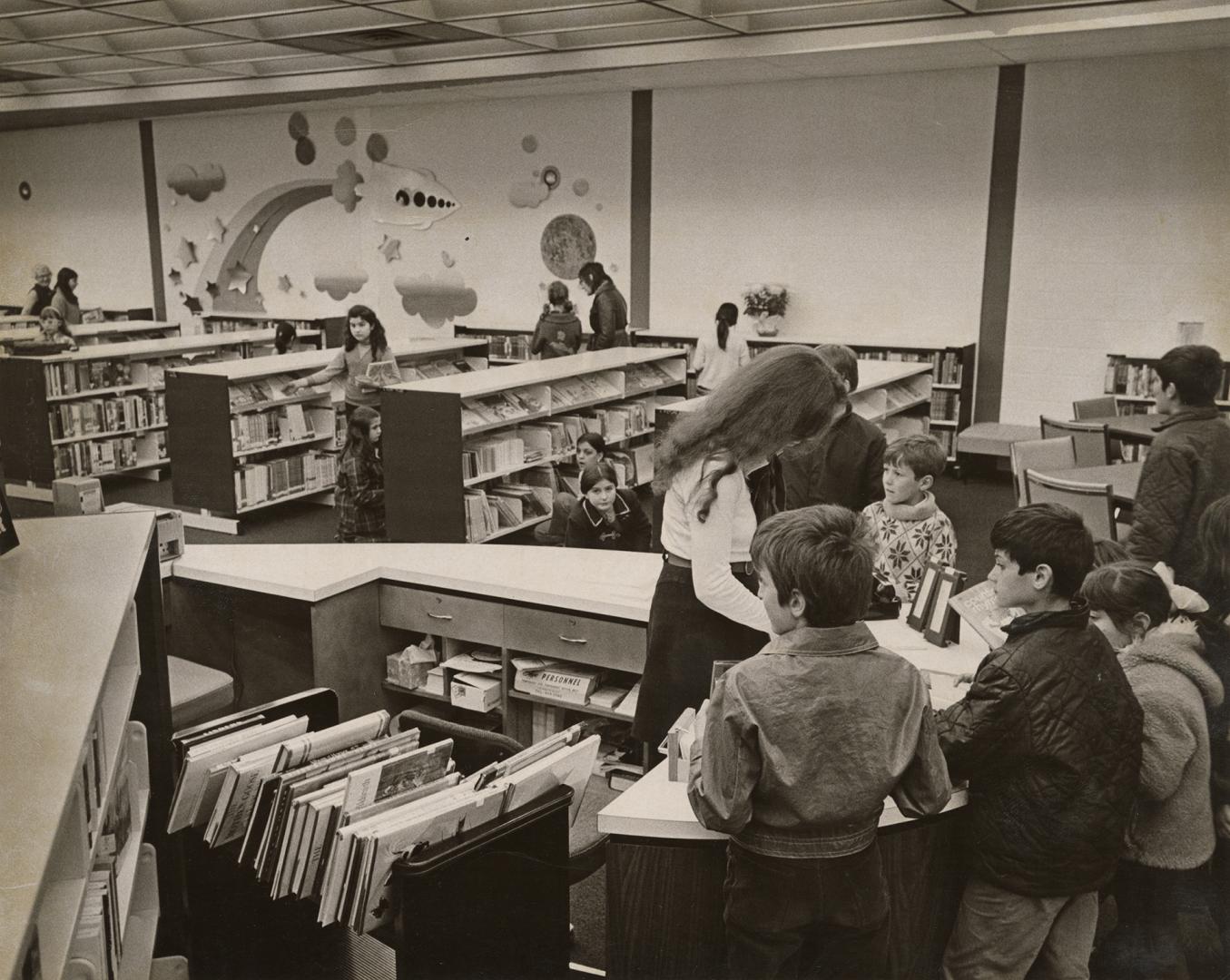 Picture of a librarian at a desk surrounded by children. 