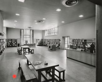 Picture of interior of a library with shelving around the walls and benches and tables. 