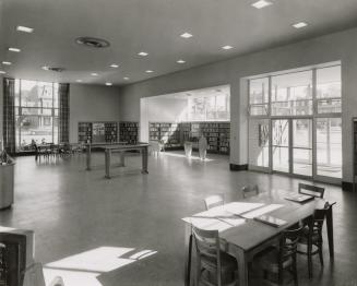 Picture of interior of a library with shelving around the walls and benches and tables. 