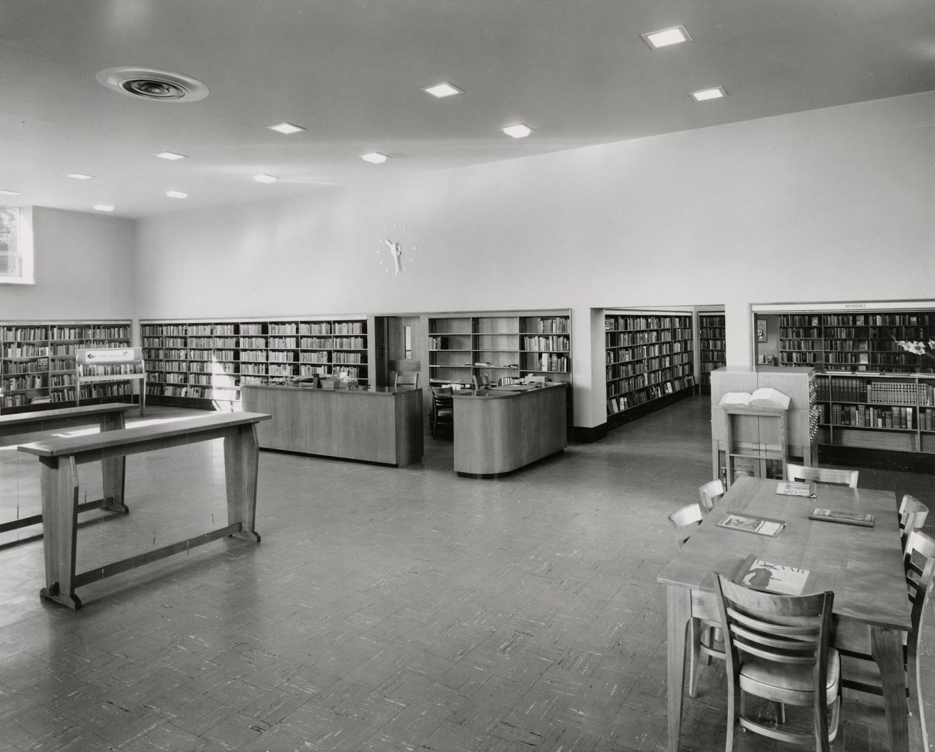 Picture of interior of a library with shelving around the walls and benches and tables. 