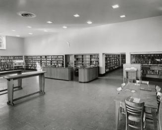 Picture of interior of a library with shelving around the walls and benches and tables. 