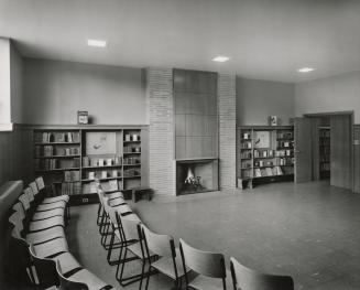 Picture of interior of a library with shelving around the walls and benches and tables. 
