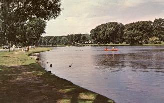 Color photograph of two people in a canoe on a river flowing through parkland.