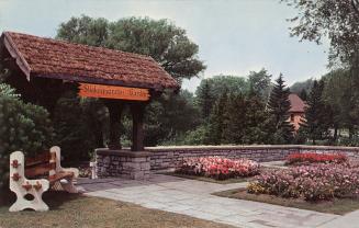 Color photograph of a park bench in front of a covered throughway of a stone wall.