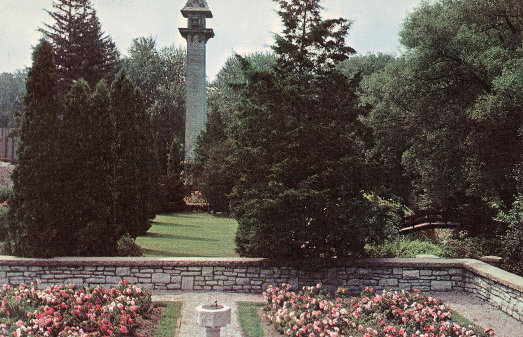 Color photograph of roses with a walled garden, chimney as a feature in the background.