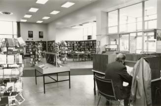 Picture of interior of library showing shelves, spinner and man at study carrel.