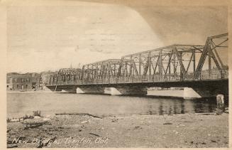 Sepia toned photograph of a long metal bridge spanning a river.