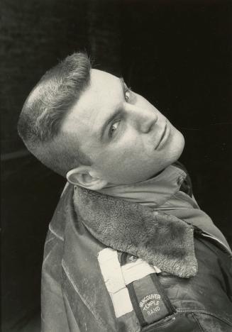 Young man with brush cut wearing old leather jacket looks up into the camera. 