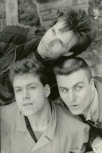Head and shoulders of three young men, two vertical on bottom and one horizontal on top. 