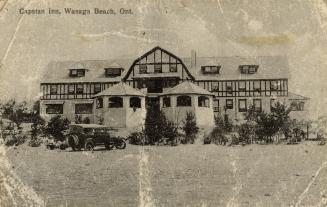 Black and white photograph of a mock-Tudor commercial building with automobiles on a beach in f…