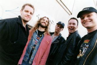 Five casually dressed young men against a white wall, shot from below waist up. 