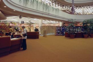 Picture of inquiry desk on main floor of large library with orange carpeting and balcony with h…