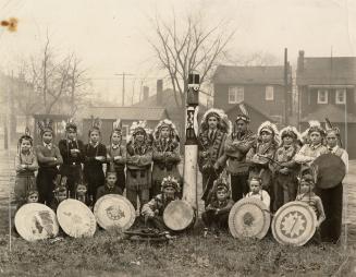  Posed photograph of twenty-one Indigenous and non-Indigenous children in native clothing and f…