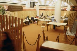 Picture of interior of a library showing customers at tables in a reading area surrounded by ar…