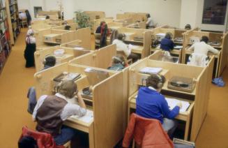 Picture of people sitting at wooden study carrels used as listening stations. 