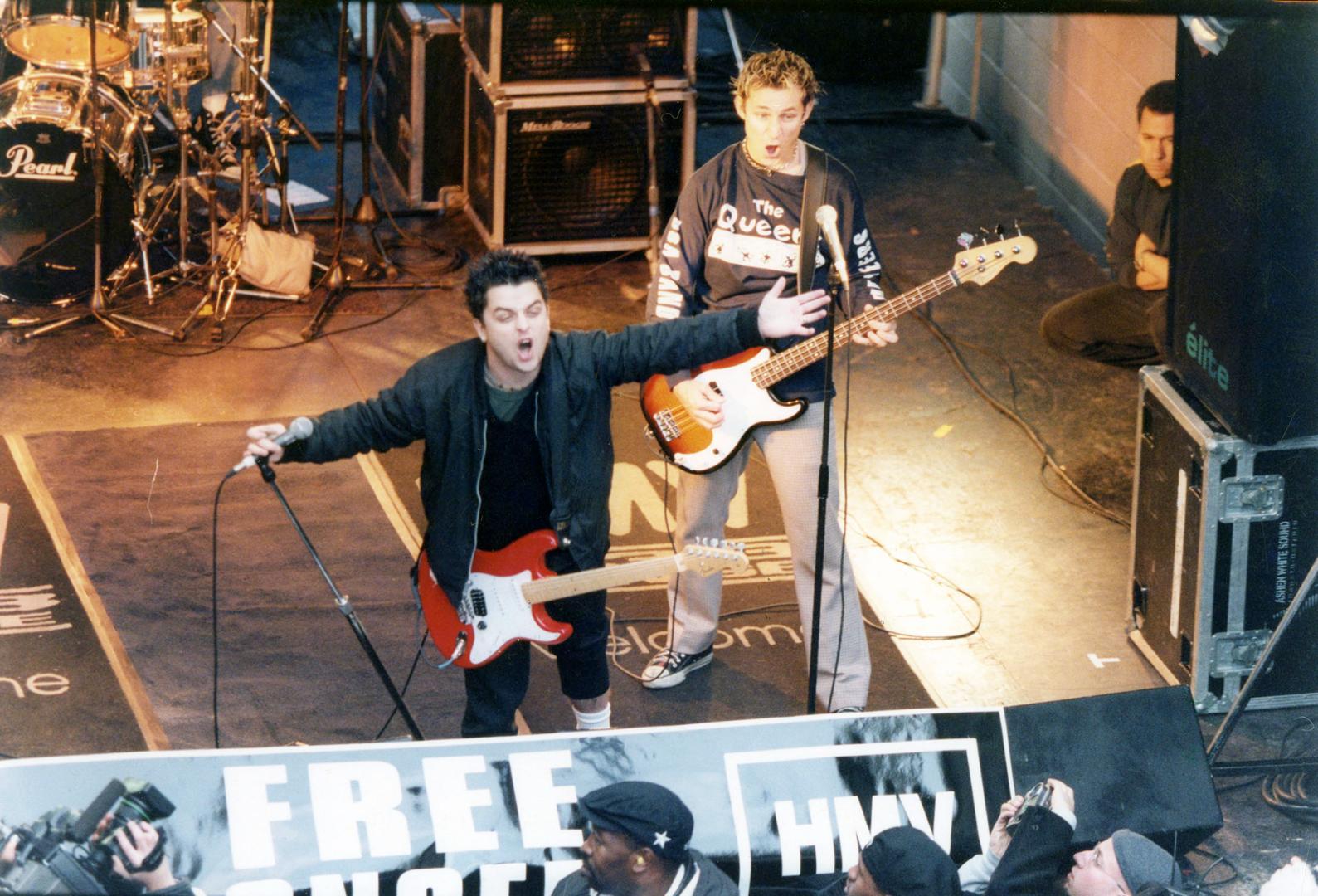On stage, lead singer with mouth wide open and guitar, arms outstretched and another guitarist …