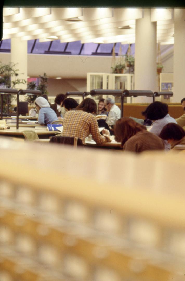 Picture people studying at tables with blurred image of card catalogue in foreground. 