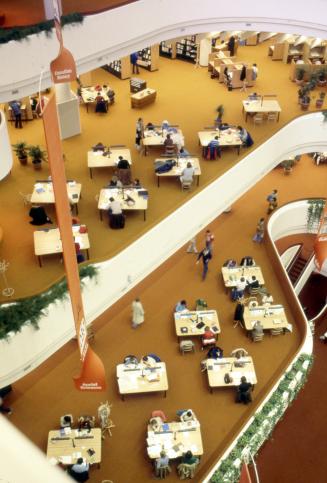 Picture looking down from a high floor at two tiers of floors with study tables n a large libra…