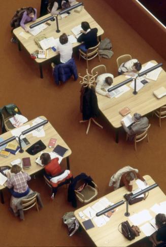 Picture looking down from above on four study tables in a library with people seated at them. 