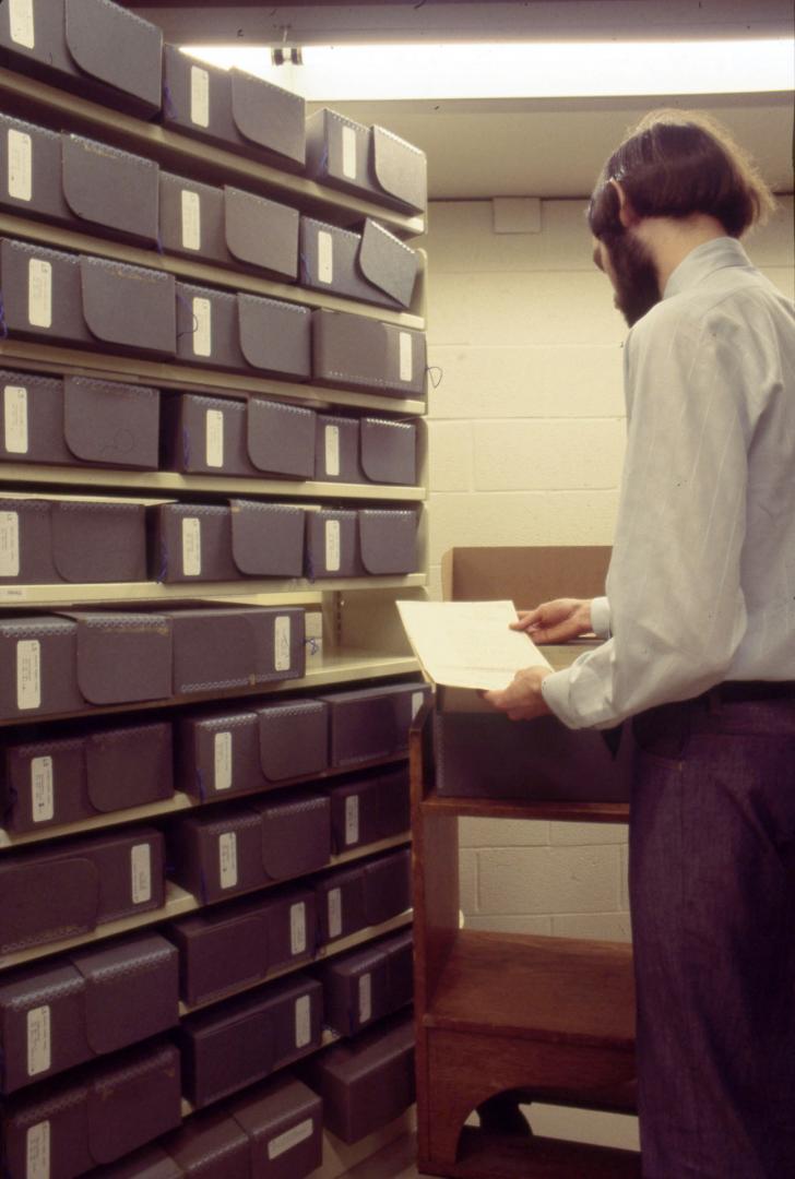 Picture of a man looking at papers from shelves of storage boxes. 