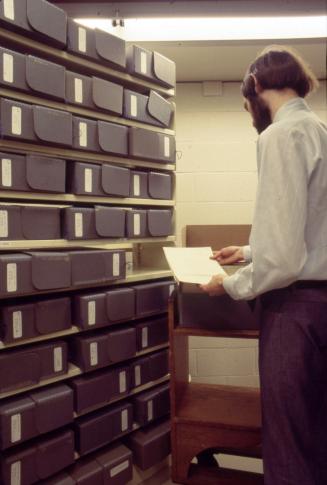 Picture of a man looking at papers from shelves of storage boxes. 