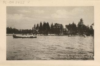 Black and white photograph of four people canoeing on a lake in front of a camp.