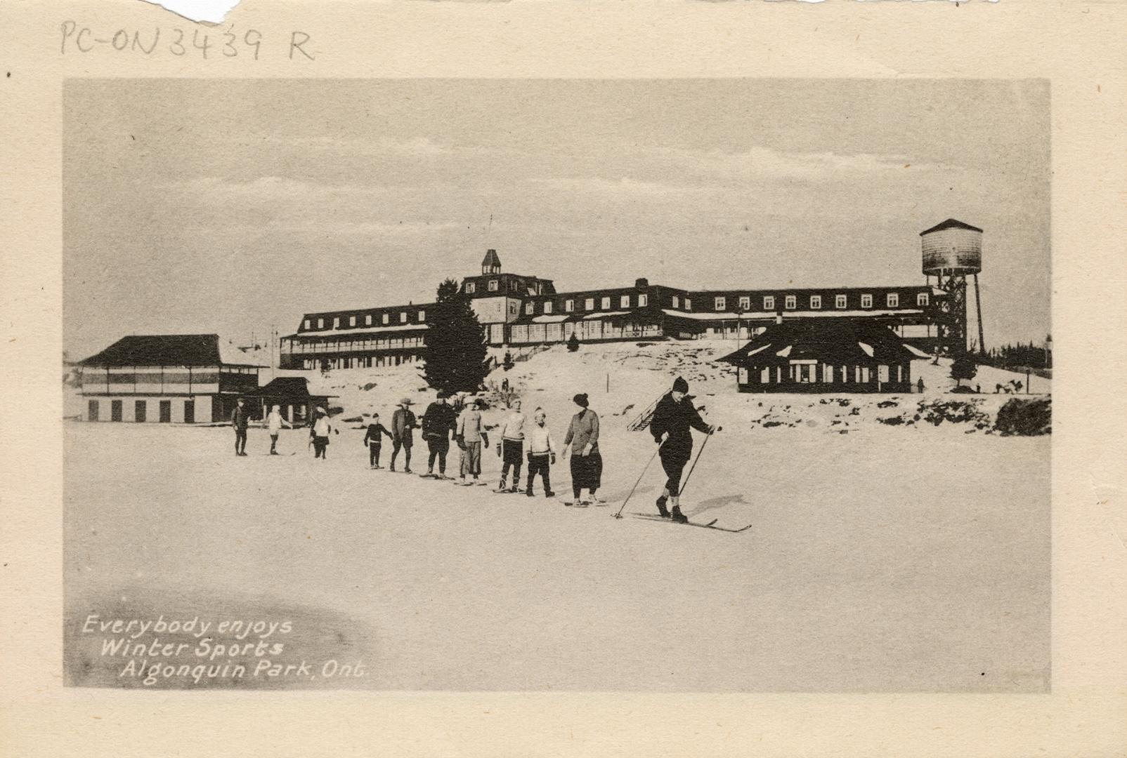 Black and white photograph of a line of cross country skiers in front of a large hotel.