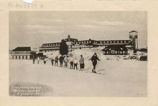 Black and white photograph of a line of cross country skiers in front of a large hotel.
