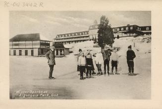 Black and white photograph of a group of people snowshoeing on ice in front of a large hotel.