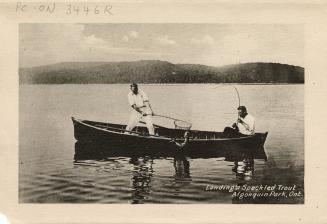 Black and white photograph of two men in a boat dip netting a caught fish.