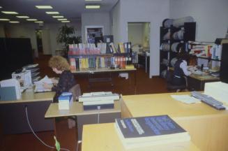 Picture of library work room with large tables and person working at a desk. 