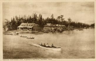 Sepia toned photograph of people in boats on water in front of a large, frame cottage.