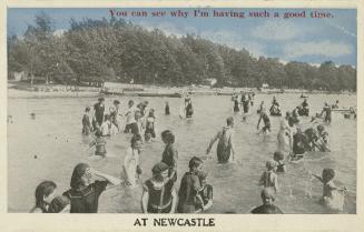 Black and white photograph of a crowd of people swimming in a lake beside a beach.