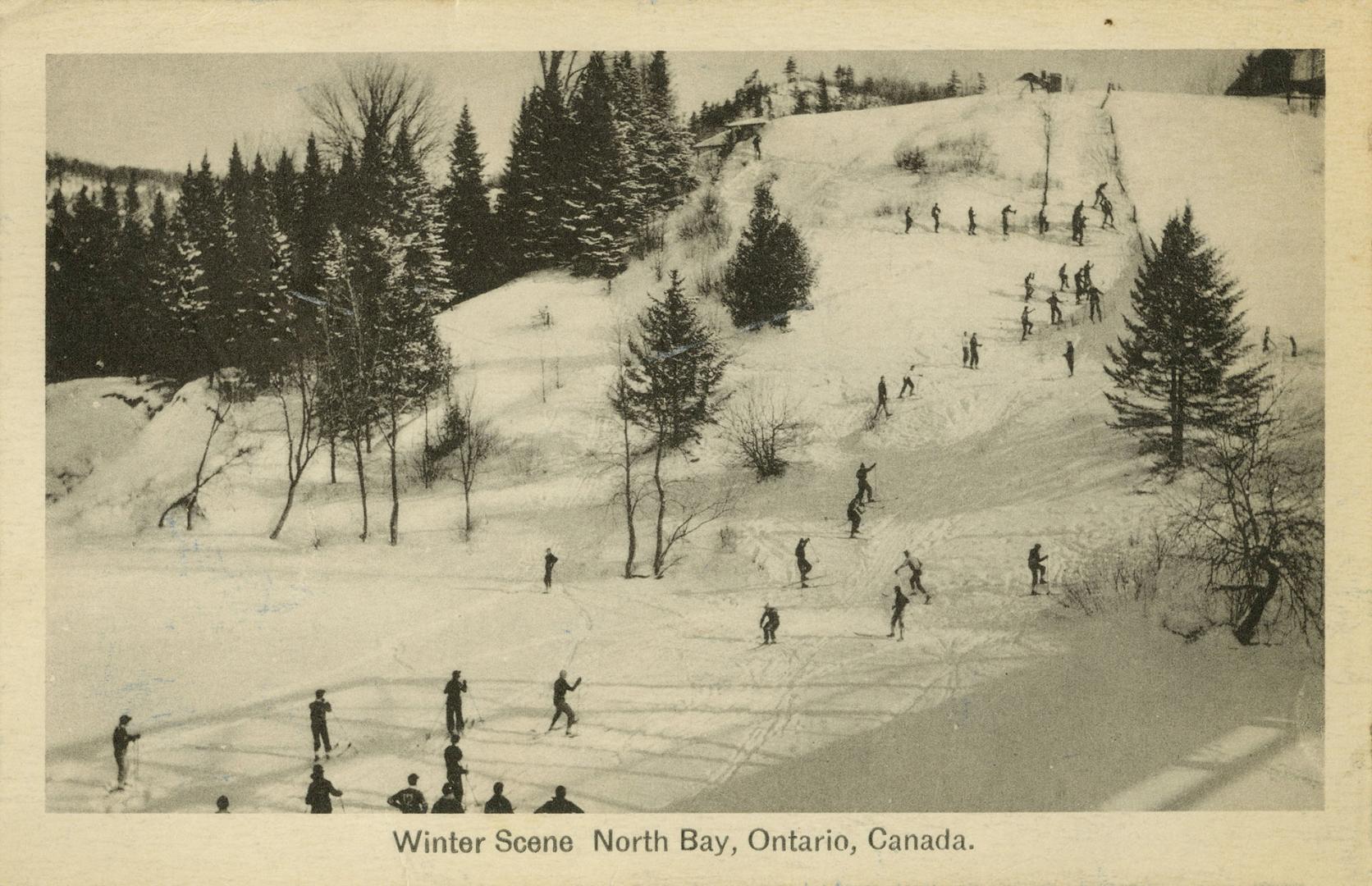 Black and white photograph of a large group of people climbing up and skiing down a hill.