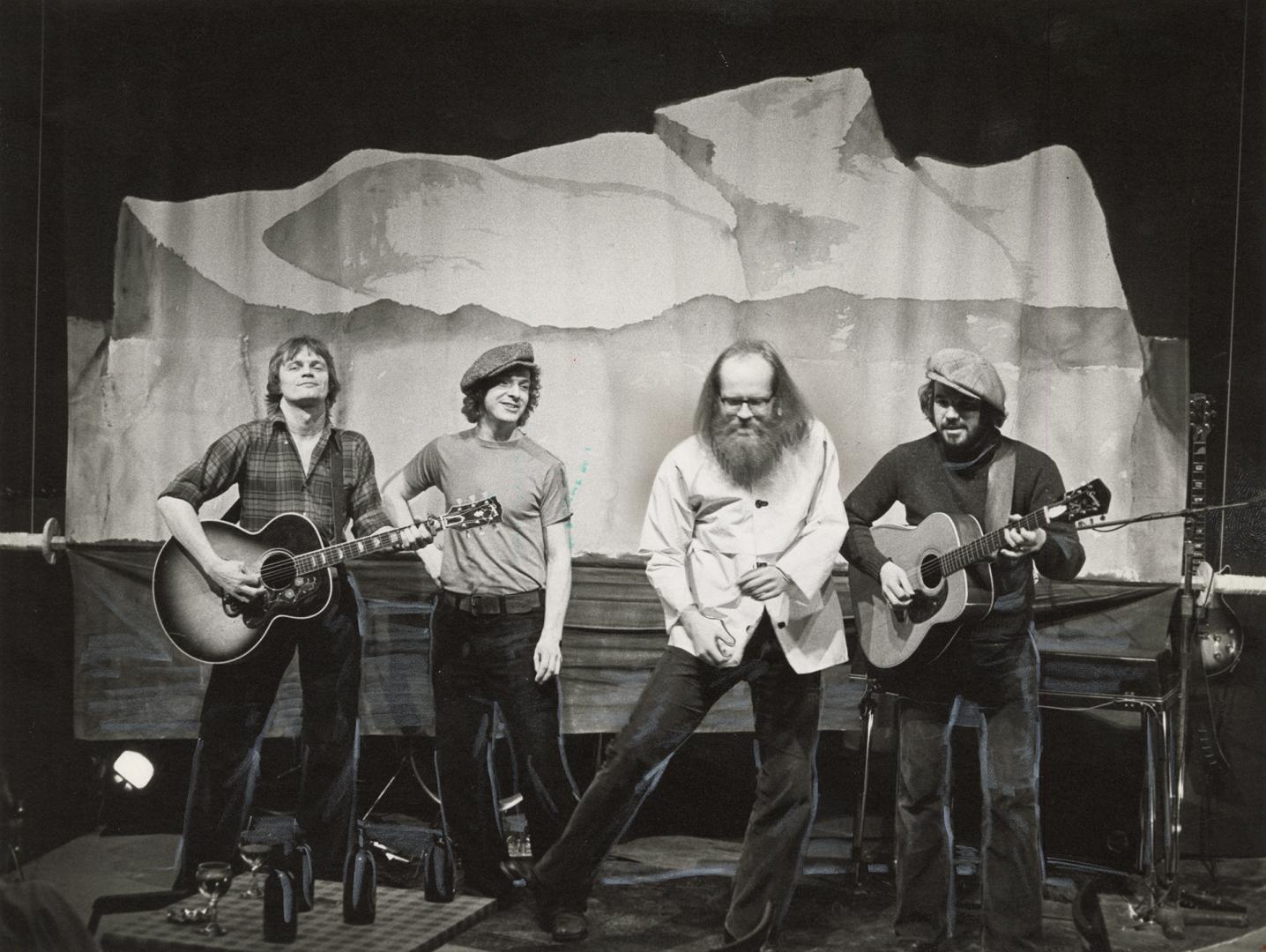 Four men onstage bull body image, all wear black velvet bell bottom pants. The two on the end p…