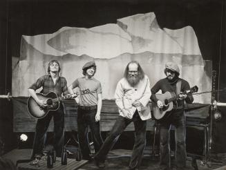 Four men onstage bull body image, all wear black velvet bell bottom pants. The two on the end p…