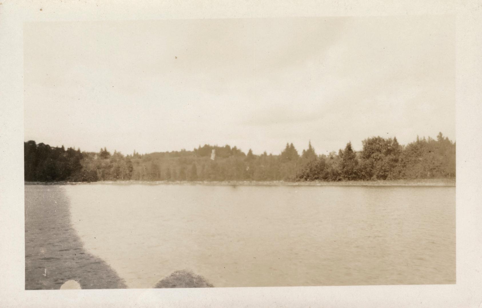 Black and white photograph of ruins taken from a boat on a body of water.