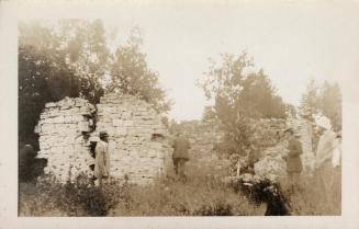 Black and white photograph of four men exploring the remains of a stone building.