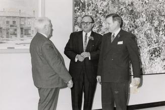 Photo of three men standing talking in front of a large abstract painting and a smaller paintin…