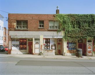 Urban scene with an old brick building, featuring ivy-covered walls and poster-adorned windows.