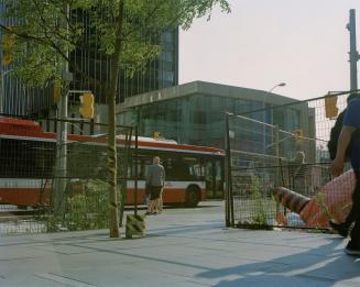 Urban intersection with a bus, construction fencing, and office buildings in the background.