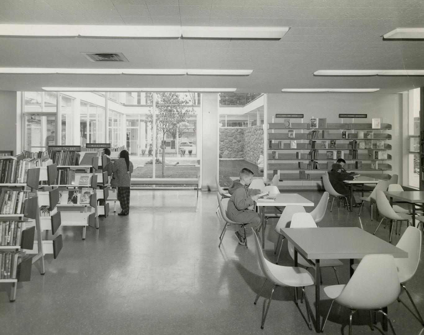 Picture of interior of library showing tables and shelves and large window to courtyard. 